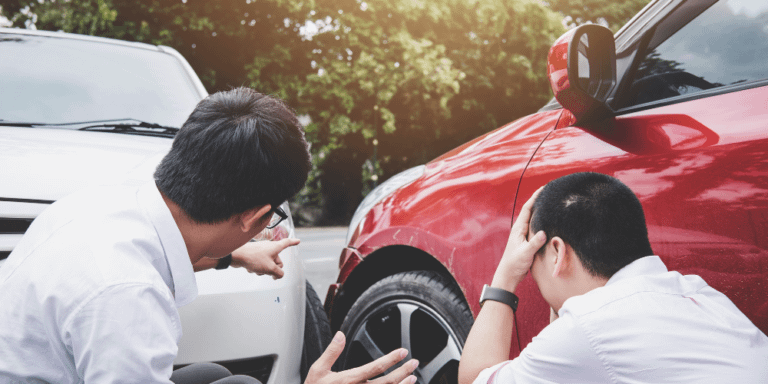 Two men examine a damaged car, discussing the extent of the damage and possible repairs.