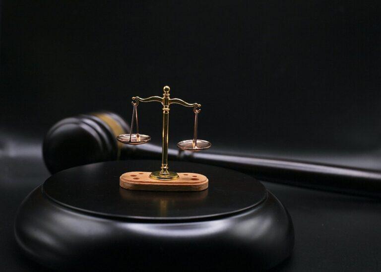 Miniature scale of justice and gavel on a black background, symbolizing law and fairness.