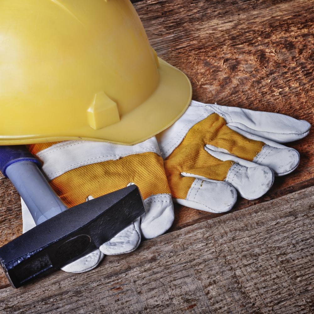 Hard hat, work gloves, and a hammer on a wooden surface
